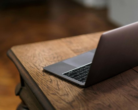 Old silver laptop open on a plain wooden desk
